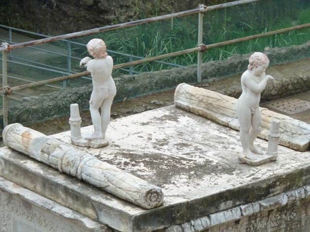 Herculaneum, September 2015. On the top of the altar stand two marble statues of sleeping funeral figures which would have been leaning on torches, but are now ruined. One of the two statues shows considerable traces of red-lead colour on their head of hair.